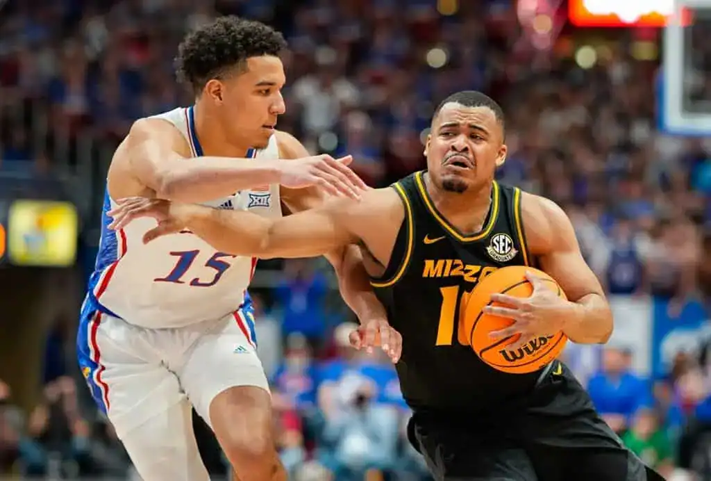 Missouri Tigers player driving to the basket with determination as a Kansas Jayhawks defender tries to guard him closely.