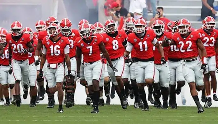 Georgia Bulldogs football players in red uniforms run onto the field together before a game.