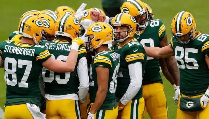 Packers players huddle together on the field during a game, strategizing before the next play.