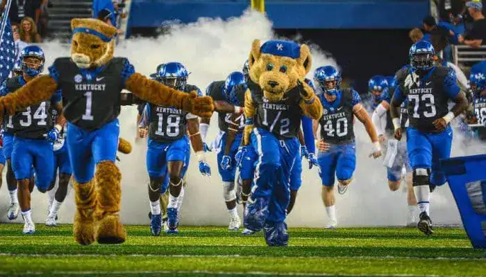 Kentucky Wildcats football team runs onto the field with mascots leading the charge through smoke.