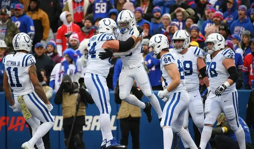 Indianapolis Colts players celebrate a touchdown on the field during an NFL game, wearing white uniforms with blue accents.