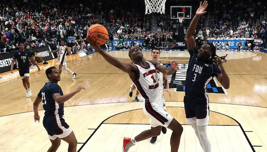 Florida Atlantic basketball player drives to the basket for a layup while a Fairleigh Dickinson defender leaps to contest the shot during a game.