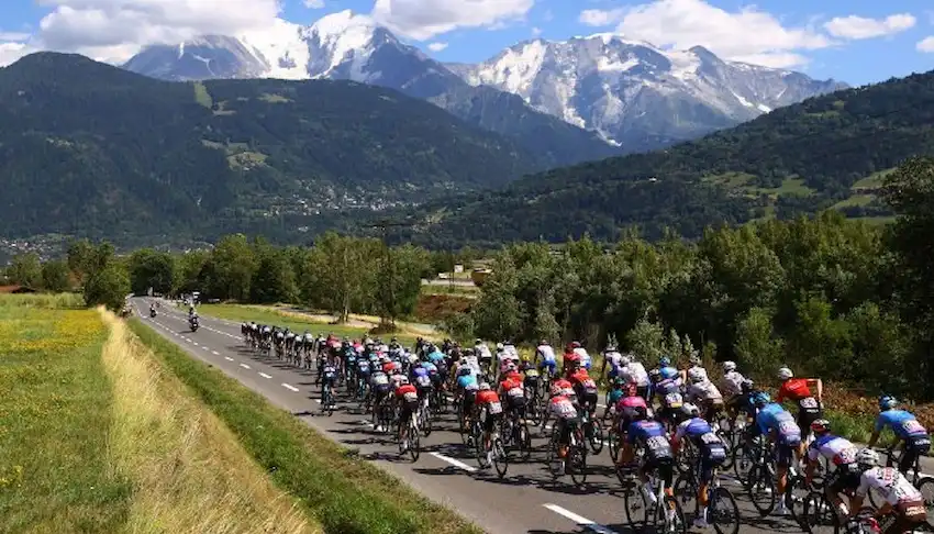 A large group of cyclists races down a scenic road.