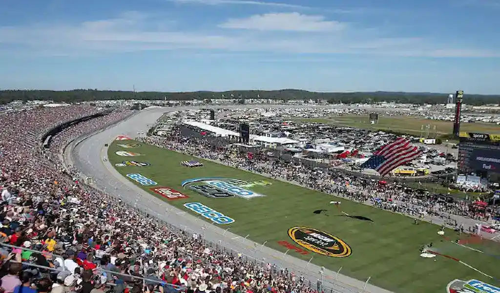 Vista panorámica de un circuito de NASCAR lleno de aficionados y con autos alineados en la pista antes de una gran carrera.