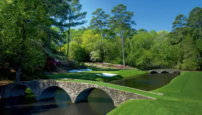 Scenic golf course view featuring a stone bridge over water with trees and flowers in the background.
