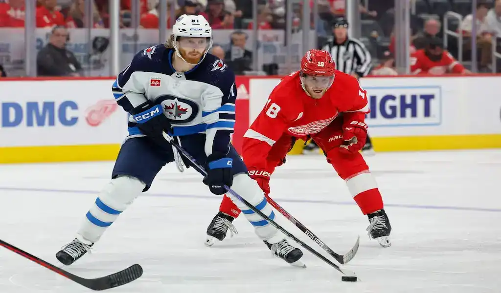 Winnipeg Jets player controls the puck while pressured by Detroit Red Wings defender during NHL action.