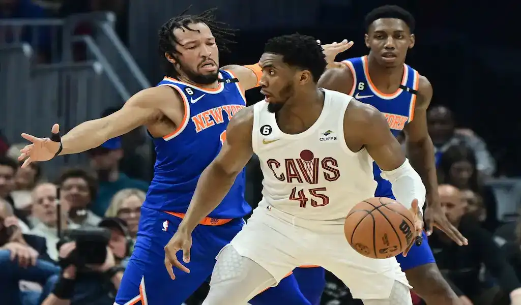 Cleveland Cavaliers player driving with the ball while being defended by New York Knicks players during an NBA game.