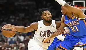 A Cleveland Cavaliers player in a wine and gold uniform with number 2 dribbling the ball, defended by an Indiana Pacers player in a blue uniform with number 23, with a blurred crowd in the background, dated October 28, 2023.