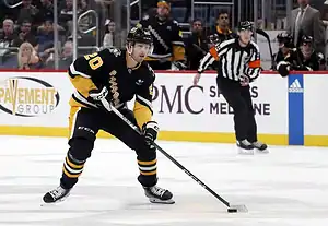 Pittsburgh Penguins hockey player in a black jersey controls the puck while skating on the ice.