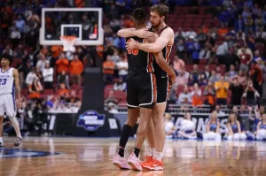 Two Princeton basketball players in black uniforms embrace on the court.