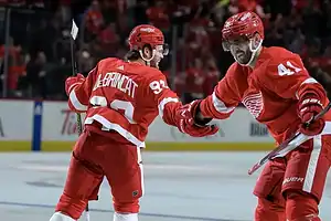 Two Detroit Red Wings players in red uniforms celebrate together on the ice.
