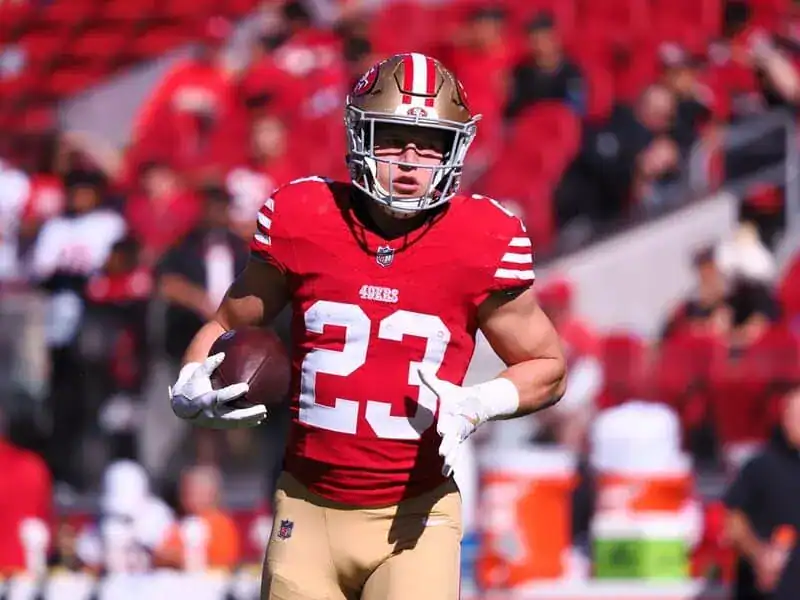 1 San Francisco 49ers player wearing jersey number 23 runs with the football during a game, with the crowd blurred in the background.