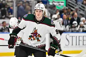 An Arizona Coyotes player skates during warmups, wearing a white jersey with the team’s coyote logo.