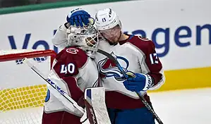 A Colorado Avalanche player with number 13 celebrating with the goalkeeper wearing number 40 near the net during a hockey game, with the rink and boards in the background.