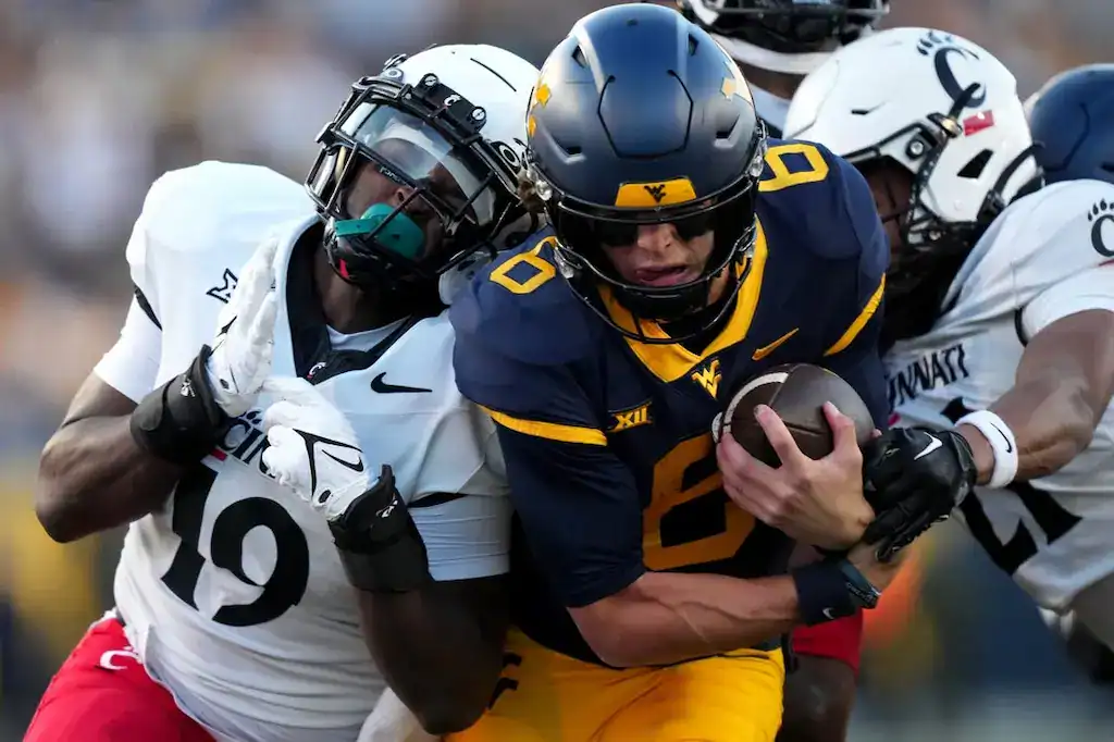 West Virginia quarterback runs while tackled by Cincinnati defenders.