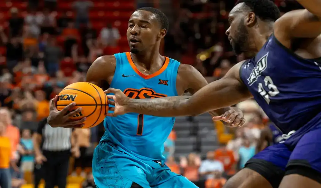 Oklahoma State Cowboys guard drives to the basket while defended by a St. Bonaventure Bonnies player during a college basketball game.