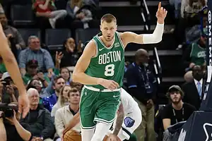 Celtics player in a green uniform raising his hand while moving up the court during an NBA game.