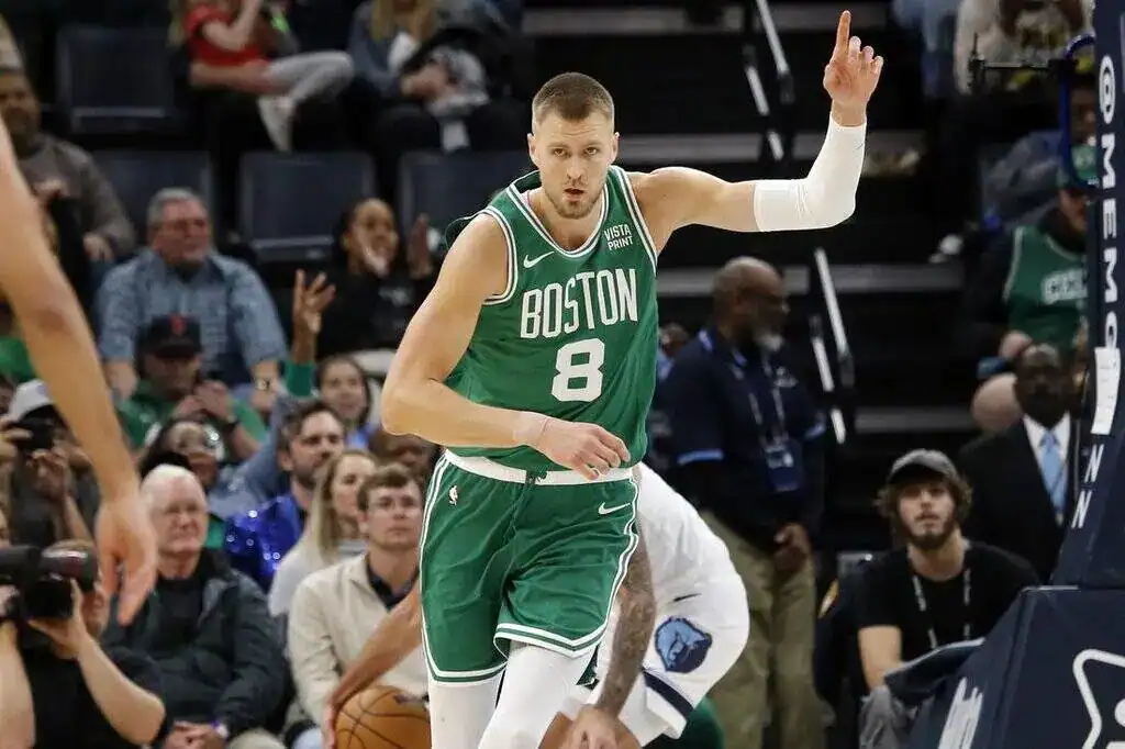 Celtics player in a green uniform raising his hand while moving up the court during an NBA game.