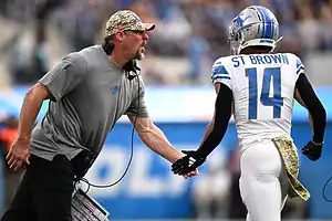 Detroit Lions coach and wide receiver Amon-Ra St. Brown exchange an intense handshake on the sideline.