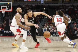 A player from the Pistons is lunging for the ball, while two Bulls players are involved in the play.