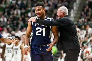 A basketball player in a Butler uniform receives guidance from a coach during an intense game, with a cheering crowd in the background.
