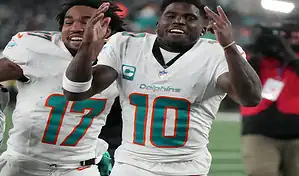 Miami Dolphins players celebrate on the field wearing white uniforms with teal and orange accents during an NFL game.