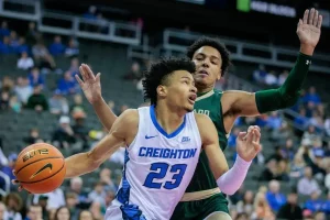 A Creighton basketball player drives to the basket while being closely guarded by a defender.
