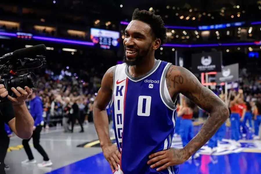 Sacramento Kings player smiling post-game, standing on the court with hands on hips while speaking to the media.