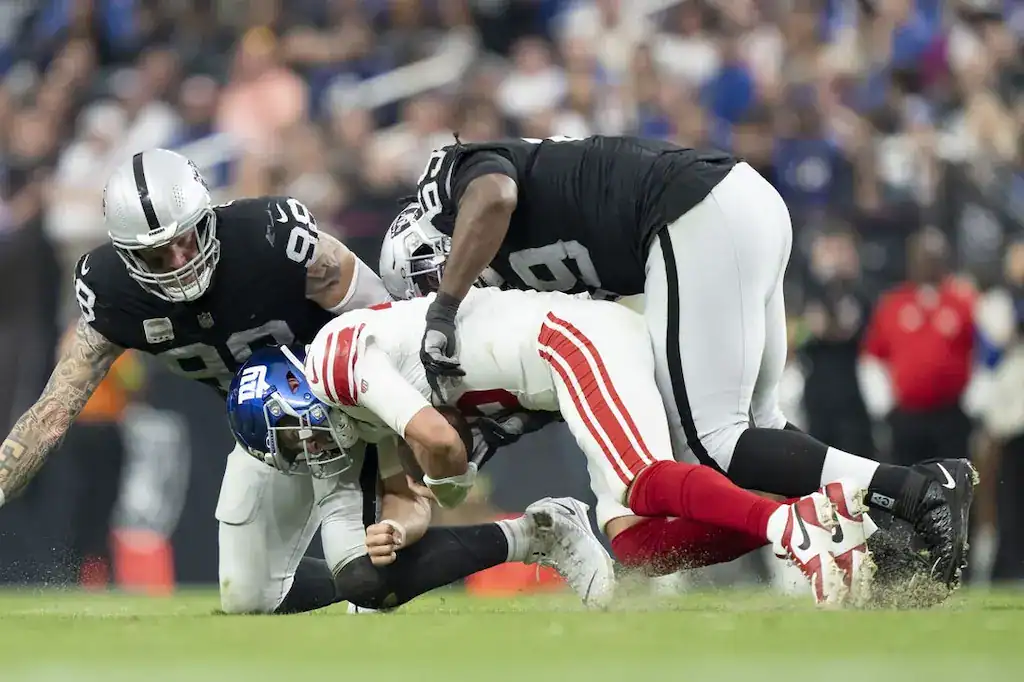 8 Las Vegas Raiders players sacking New York Giants quarterback during an NFL game