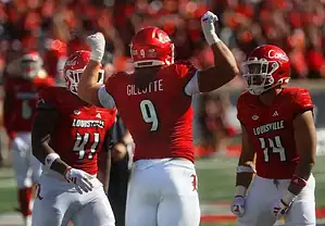 Louisville Cardinals football players in red uniforms celebrate together after a play.
