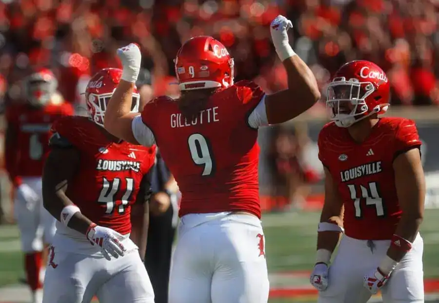Louisville Cardinals football players in red uniforms celebrate together after a play.