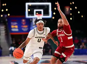 A Michigan basketball player dribbles past a Stanford defender during a game, showcasing action and athleticism on the court.