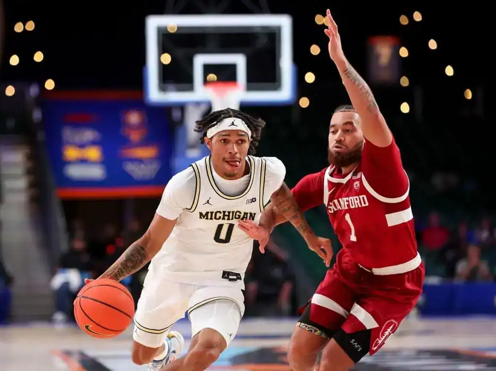 A Michigan basketball player dribbles past a Stanford defender during a game, showcasing action and athleticism on the court.