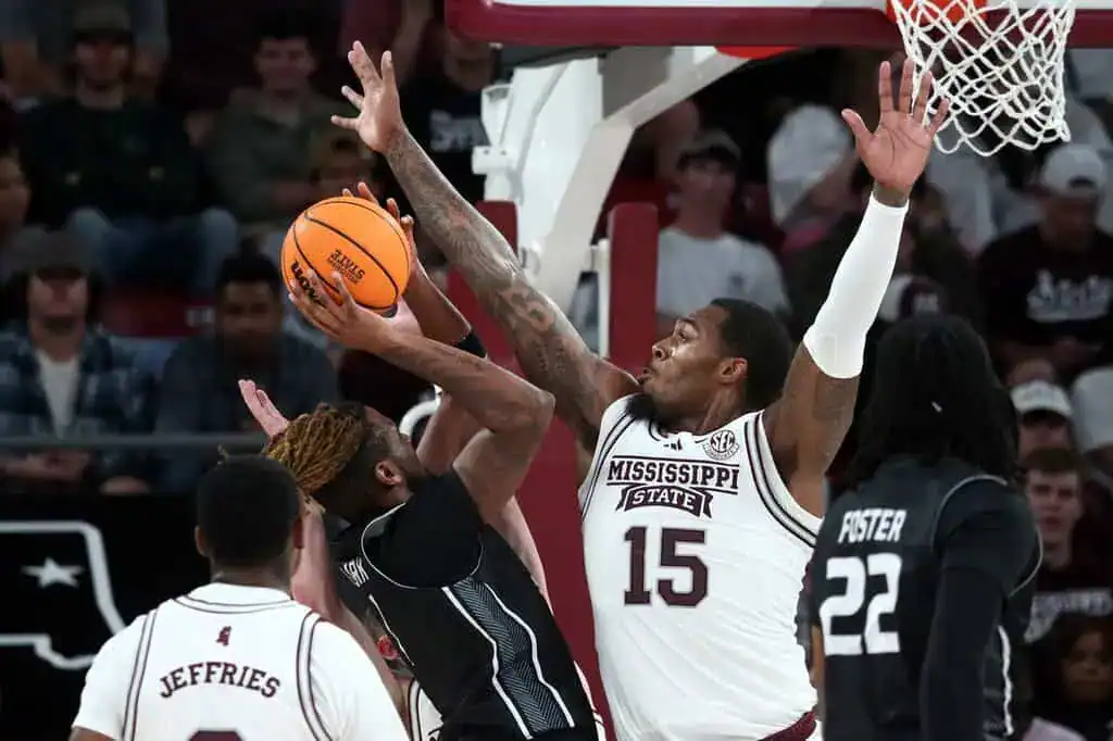 A Mississippi State basketball player wearing jersey number 15 blocks a shot from an opposing player during a game. Other players are visible in the background.