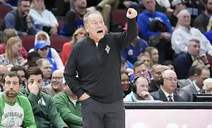 College basketball coach animatedly pointing and giving instructions from the sideline during a game.