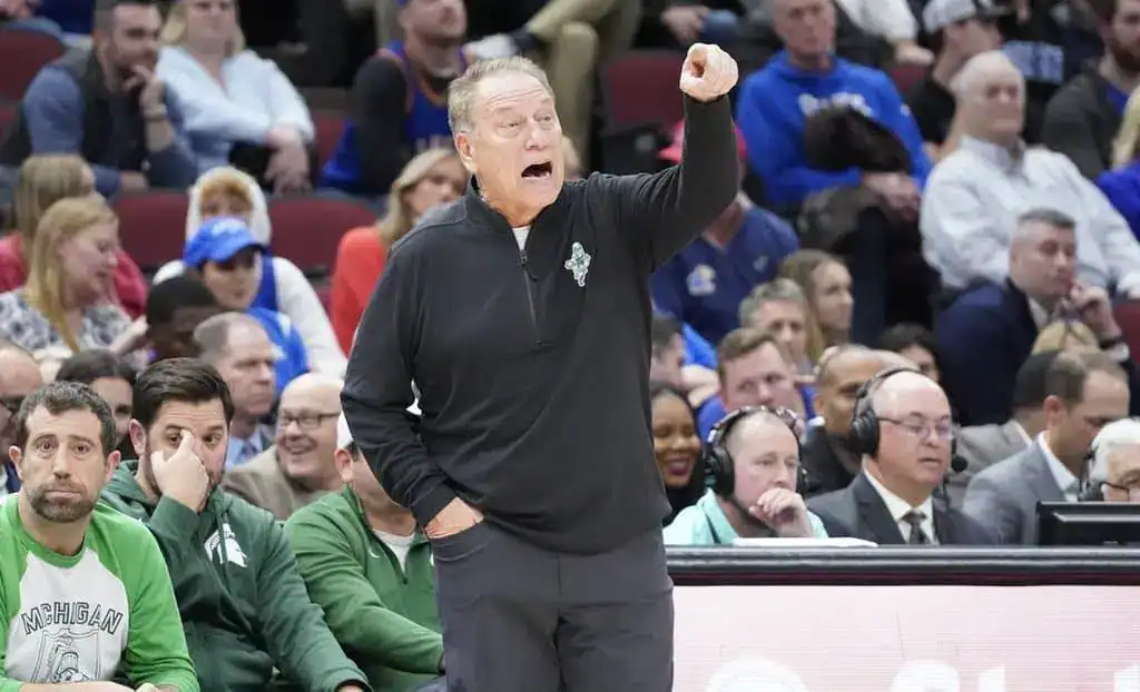 College basketball coach animatedly pointing and giving instructions from the sideline during a game.