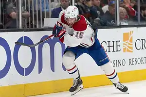 Montreal Canadiens player skating aggressively along the boards, holding his stick while wearing a white jersey with red and blue accents.