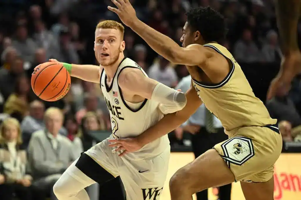 A college basketball player drives past a defender while dribbling during a game.