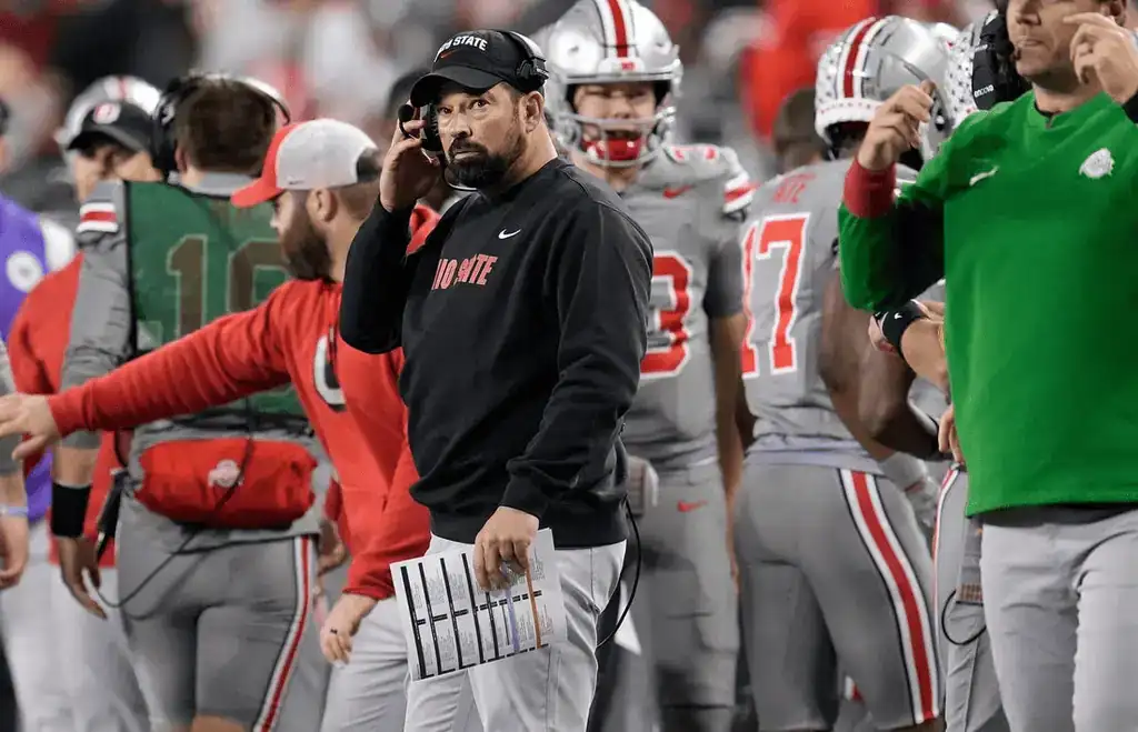 Ohio State coach with players on sideline during game.