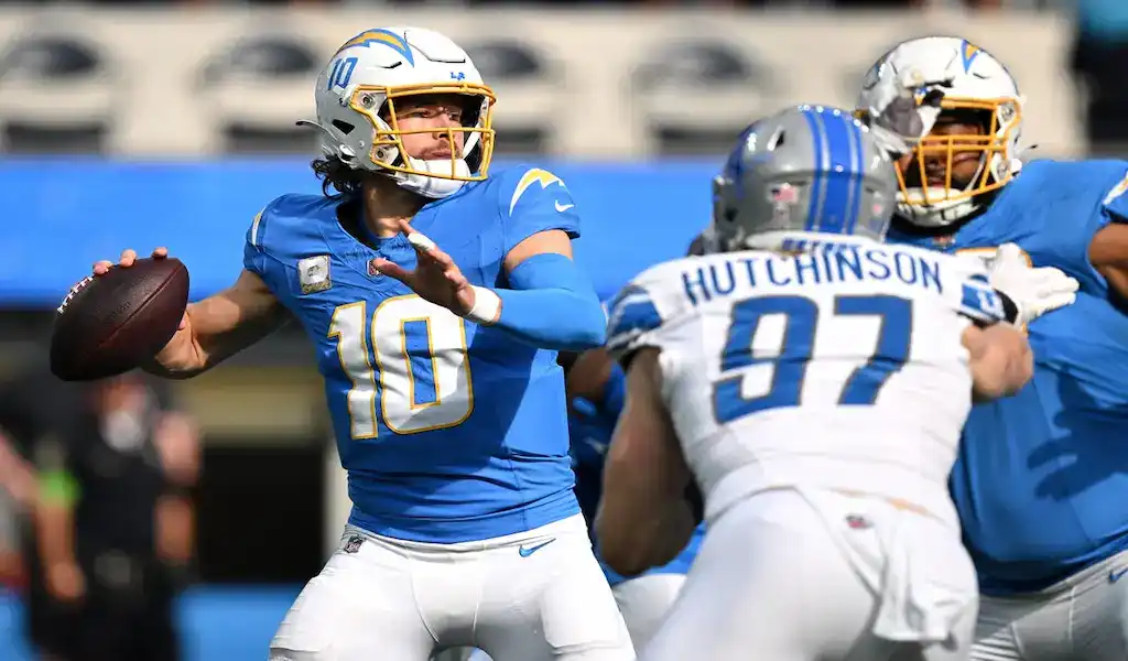 Los Angeles Chargers quarterback prepares to throw a pass while pressured by Detroit Lions defender during NFL action.