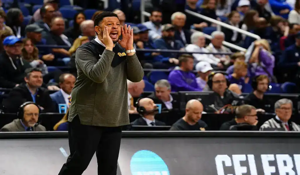 Pittsburgh Panthers coach shouts instructions from the sideline during NCAA basketball game against Jacksonville Dolphins.