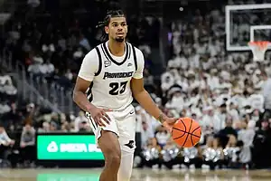 Providence Friars basketball player in a white uniform dribbles the ball while looking to set up a play.