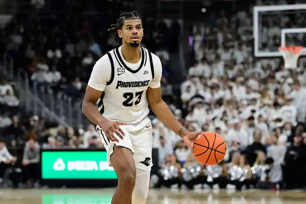 Providence Friars basketball player in a white uniform dribbles the ball while looking to set up a play.