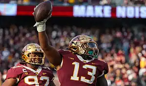 Minnesota Golden Gophers football player raises the ball in celebration during a game against the Purdue Boilermakers.
