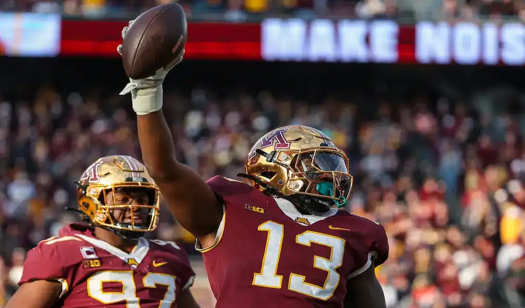 Minnesota Golden Gophers football player raises the ball in celebration during a game against the Purdue Boilermakers.
