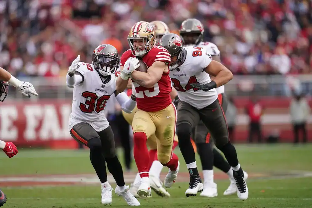 49ers running back Christian McCaffrey runs with the ball, pursued by Buccaneers defenders.