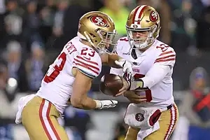 San Francisco 49ers quarterback hands the football to running back Christian McCaffrey in an NFL matchup under bright stadium lights