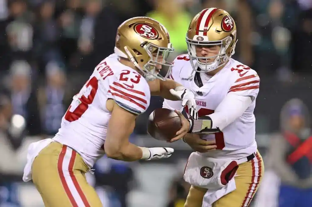 San Francisco 49ers quarterback hands the football to running back Christian McCaffrey in an NFL matchup under bright stadium lights
