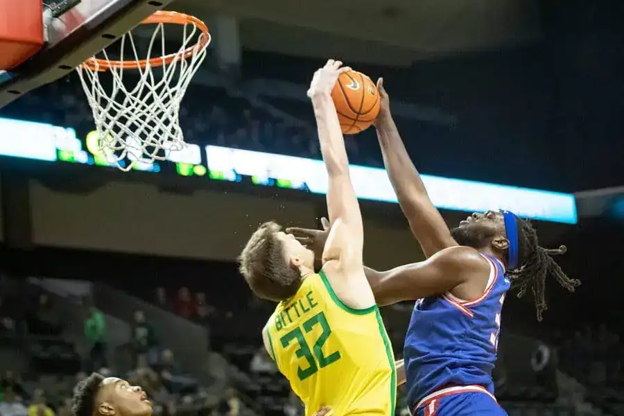 Oregon Ducks player attempting to block a shot from an opposing player during an intense basketball game.