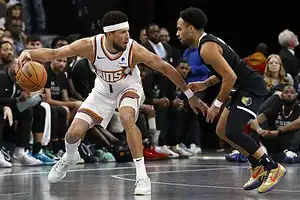 Phoenix Suns player Devin Booker dribbles against Memphis Grizzlies defender.